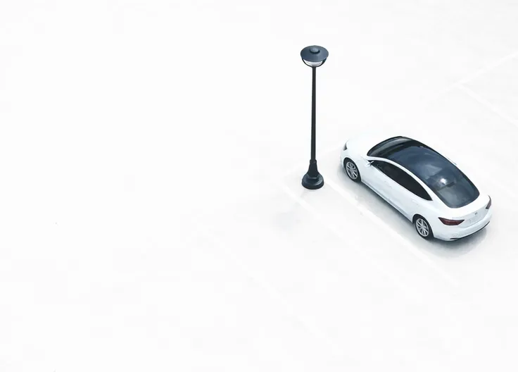 En hvit bil parkert ved en lyktestolpe på en privat parkeringsplass.